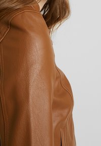 Brun læderjakke med en struktureret finish, der har et struktureret design og synlige syninger langs skulderen.