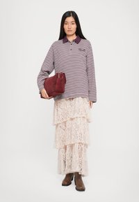 Gestreiftes langärmliges Poloshirt in Weinrot und Weiß, geschichteter Spitzenrock in Hellrosa, braune Stiefeletten und eine burgunderfarbene Wildlederhandtasche.