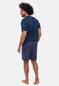 Marineblauw T-shirt met korte mouwen, gecombineerd met gestreepte shorts in verschillende kleuren. Het model staat blootvoets, wat de relaxte uitstraling benadrukt.
