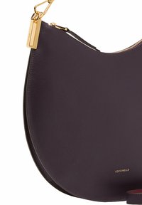 Bolso de hombro de piel en color morado oscuro con forma redondeada, herrajes dorados y un logo sutil. Textura suave con cierre de cremallera.