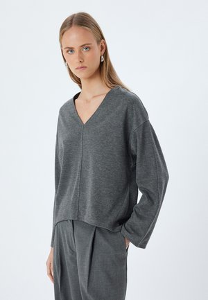 Maglia grigia a maniche lunghe con scollo a V e vestibilità comoda, realizzata in tessuto morbido, presenta spalle scese e orlo leggermente corto. Abbinata a pantaloni grigi.