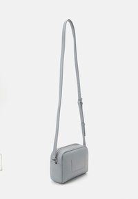 Světle šedá crossbody taška, obdélníkový tvar, hladká kožená úprava, nastavitelný popruh, horní zipové uzavření, drobné embosované detaily na přední straně.