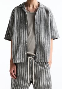 Chemise à manches courtes rayée gris et blanc, avec col, boutons sur le devant et coupe décontractée, assortie à un pantalon rayé assorti.
