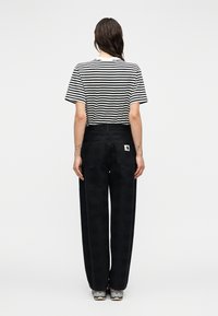 Μαύρο τζιν φαρδιάς γραμμής με τετραγωνισμένο σχέδιο, φορεμένο με μαύρο-λευκό ριγωτό μπλουζάκι. Διαθέτει πίσω τσέπη και ετικέτα στη μέση.