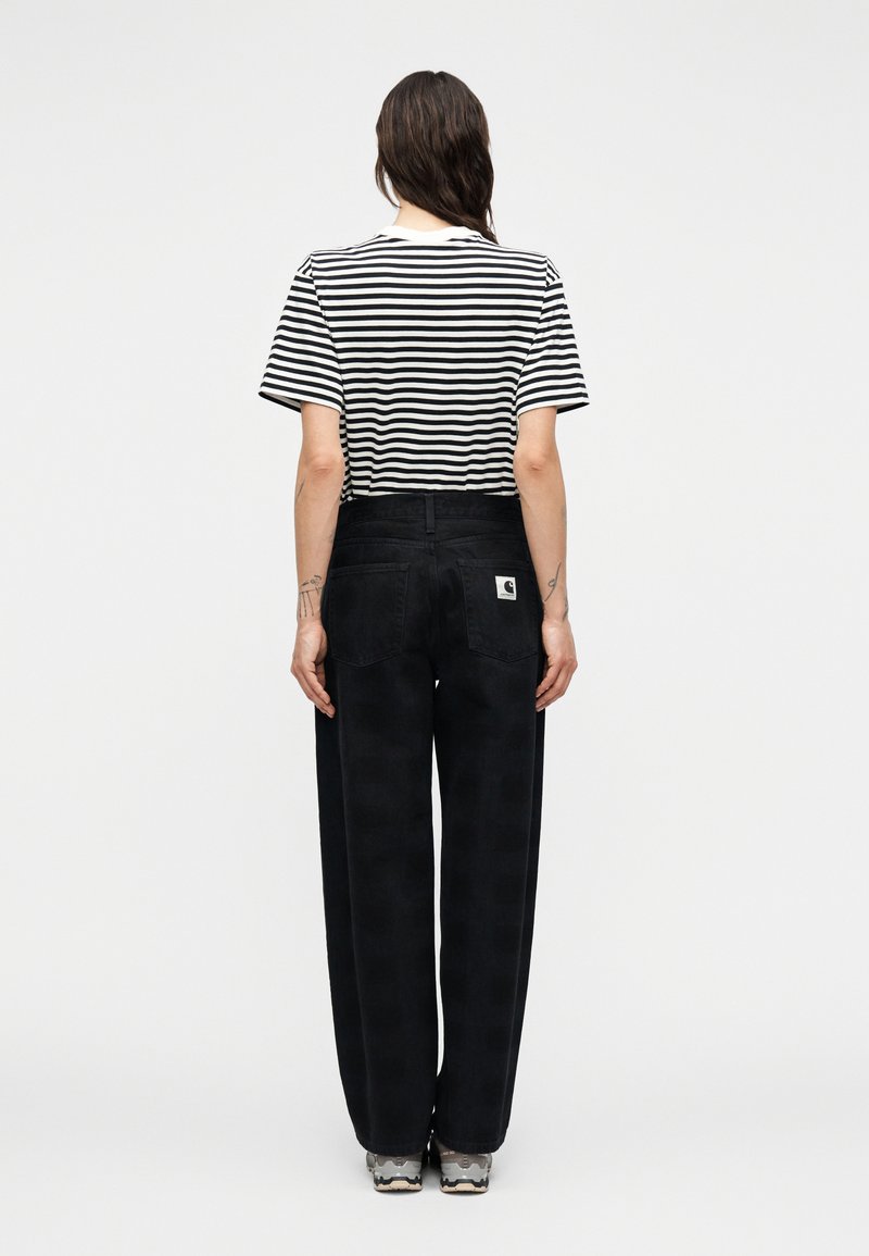 Jeans neri a gamba larga con motivo a quadri, indossati con una maglietta a righe bianca e nera. Presentano una tasca posteriore e un'etichetta sulla cintura.