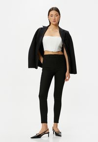Jeans ajustados negros combinados con una blusa sin tirantes blanca y un blazer negro de gran tamaño. Completado con zapatos de tacón negro puntiagudos.