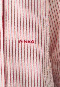 Tessuto bianco con strisce verticali rosse; presenta il nome del marchio "PINKO" ricamato in rosso vicino al colletto. Superficie testurizzata.