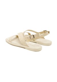 Beige sandal featuring wide crisscross straps with a textured finish and a metallic buckle. Flat sole with a smooth surface.
