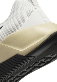 White athletic shoe featuring a mesh upper, synthetic toe cap, beige midsole, and a textured black rubber outsole with grip patterns.