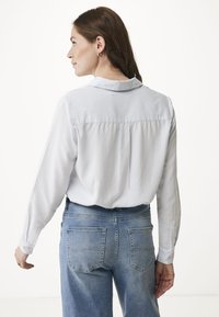 Vit långärmad blus med krage, med en ryggsöm och veck. Kombinerad med ljusblå hög midja denimjeans, med standardfickor.