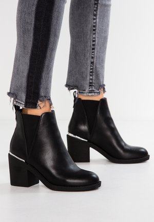 Bottines en cuir noir avec un bout arrondi, des panneaux latéraux en élastique et un accent argenté sur le talon. Associé avec un jean gris effiloché.