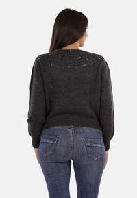 Maglione grigio scuro con maniche lunghe, tessuto testurizzato e dettagli decorativi in perline sulla parte superiore della schiena. Abbinato a jeans blu scuro.