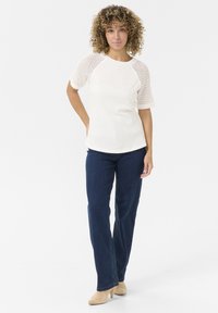 Haut blanc à manches courtes avec des manches en maille texturée, associé à un jean droit bleu foncé. La tenue présente une coupe décontractée et un design simple.
