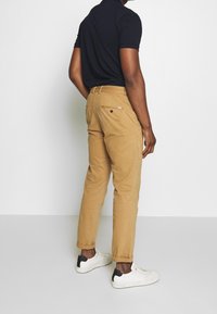 Chinos beiges slim fit, avec des poches arrière et des détails surpiqués. Associés à des baskets blanches avec des accents noirs.
