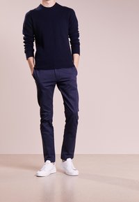 Granatowy sweter z dzianiny z prążkowymi mankietami, zestawiony z granatowymi chinosami i białymi trampkami. Strój cechuje się prostym, klasycznym wzorem.