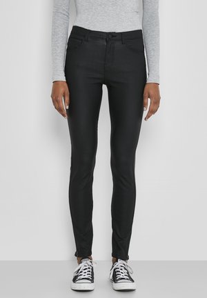 Zwarte slim-fit jeans met een zachte textuur, middelhoge taille, steekzakken en ritsen bij de enkel; gecombineerd met zwarte sneakers.