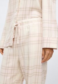 Rutete loungewear sett i myk, lys beige med rosa og grå toner. Har knyte topp med knapp og bukser med elastisk midje og snøring.