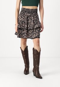 Black floral layered skirt with light pink flowers, smocked waist, and scalloped hem, paired with brown leather cowboy boots with heels.