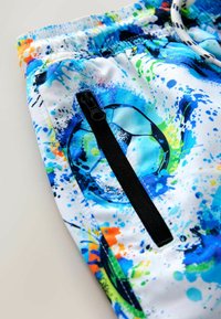 Kleurrijke strandshorts met een witte basis en blauwe, groene en oranje spetters, zwarte ritszak en elastische tailleband.