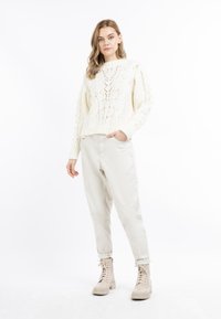 Pull en tricot crème avec des motifs texturés, associé à un pantalon tapered beige clair et des bottines à lacets beiges.