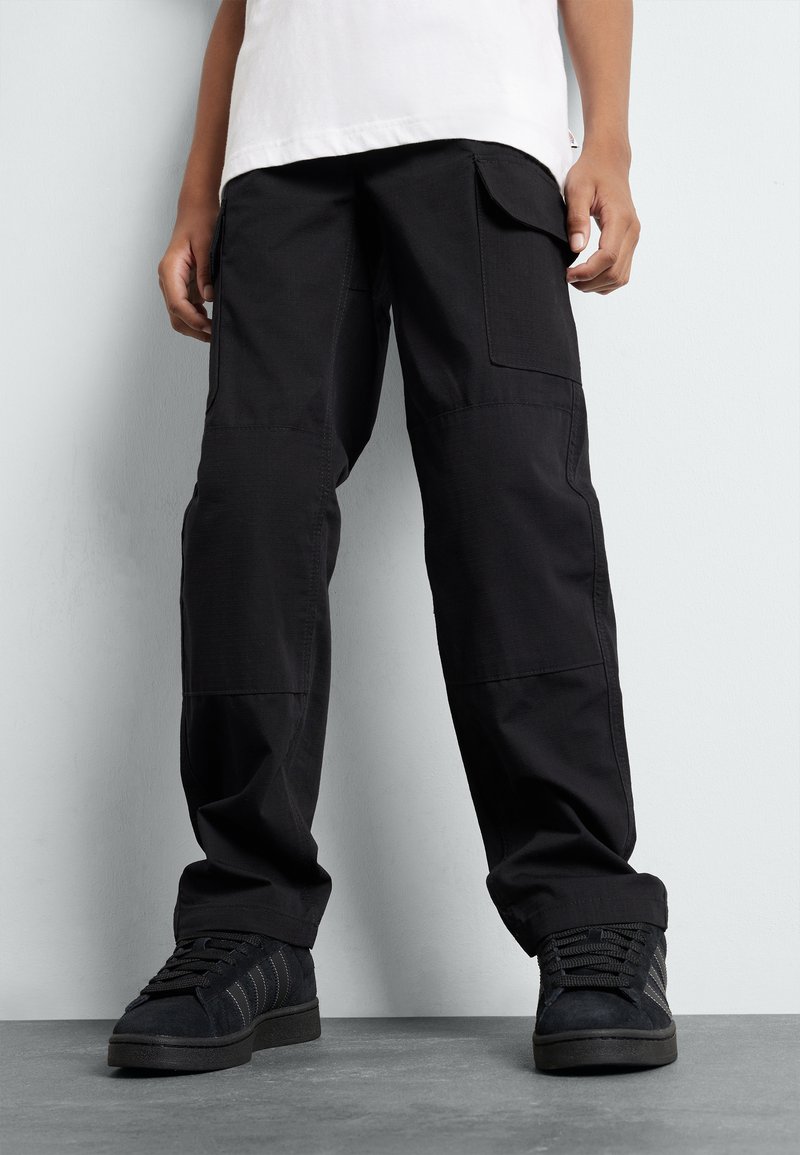Black cargo pants with a relaxed fit, featuring patch pockets, a smooth texture, and reinforced knee panels. Paired with black sneakers.