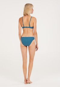 Bikini set u tirkiznoj boji s rebrastom teksturom, koji sadrži bralette top s tankim trakama i odgovarajuće donje dijelove niskog struka. Mekana tekstura s minimalističkim dizajnom.