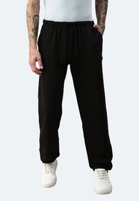 Schwarze Jogginghosen mit elastischem Bund und Kordelzug, ausgestattet mit Seitentaschen und einem lockeren Schnitt, kombiniert mit weißen Turnschuhen.