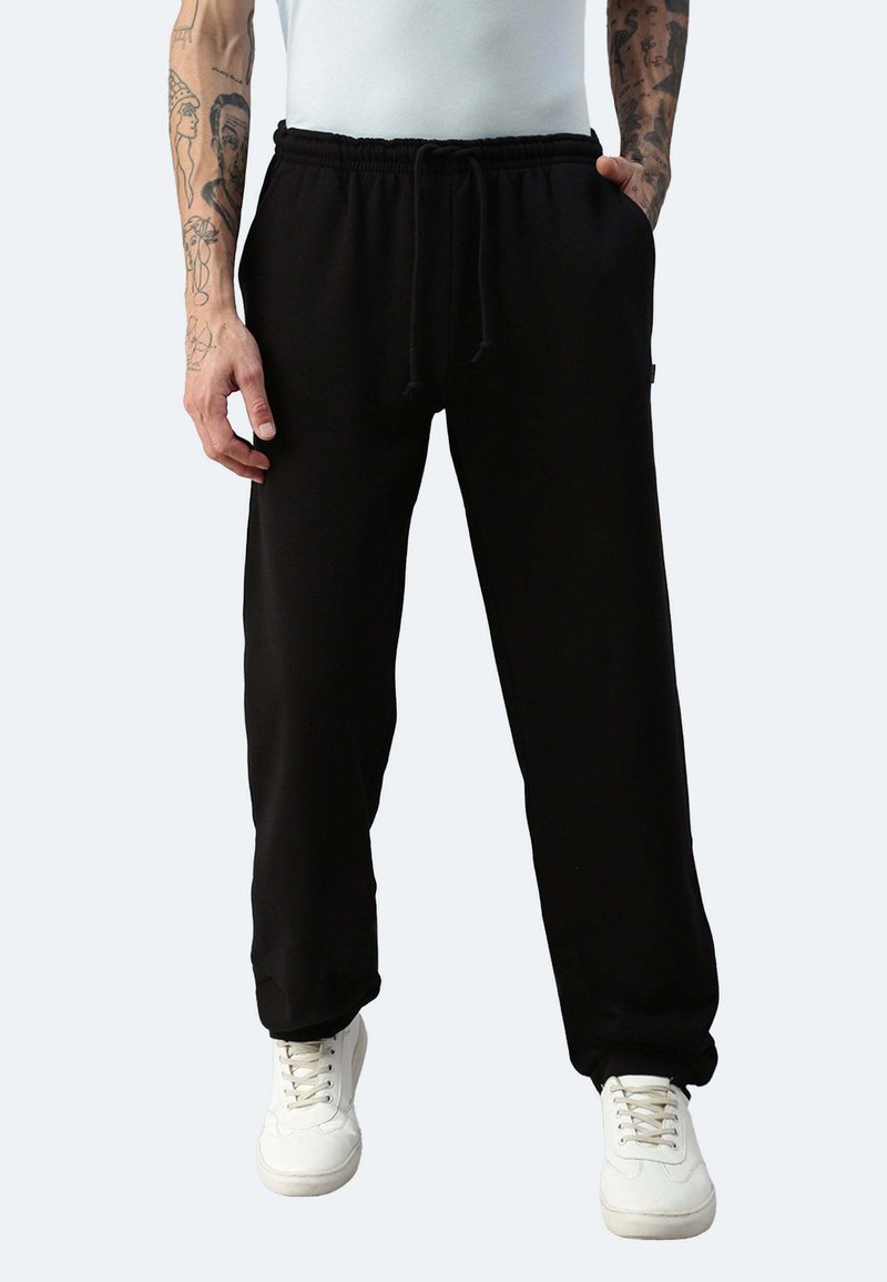Schwarze Jogginghosen mit elastischem Bund und Kordelzug, ausgestattet mit Seitentaschen und einem lockeren Schnitt, kombiniert mit weißen Turnschuhen.
