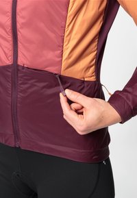 Lehká bunda s barevnými bloky v maroon, broskvové a oranžové barvě. Obsahuje zipovou kapsu a elastické manžety. Hladký nylonový materiál.