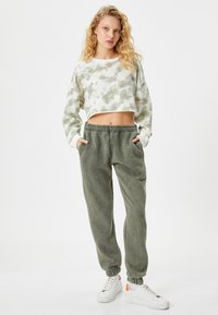 Przycięty, tye-dye sweatshirt w jasnym zielonym i białym kolorze, sparowany z pasującymi zielonymi dresami. Dresy mają elastyczne mankiety i boczne kieszenie. Białe sneakersy.
