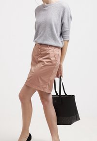 Maglione grigio chiaro a maniche corte abbinato a una gonna rosa fino al ginocchio. La modella tiene una borsa a tracolla nera con un accento di borchie.