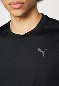 T-shirt atletica nera con maniche corte, caratterizzata da un logo Puma grigio discreto sul petto sinistro, realizzata in un tessuto morbido e leggero.