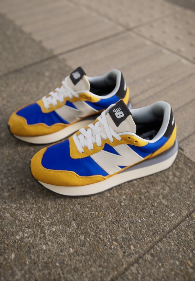 Blauwe, gele en witte sneaker van suède en mesh materialen, met een textuur op de zool, traditionele vetersluiting en logo op de tong.