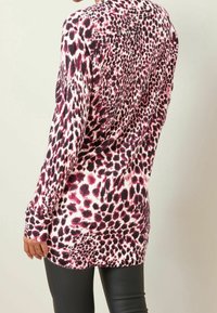 T-shirt à manches longues présentant un motif léopard rose et noir, fabriqué en matériau doux, avec une coupe décontractée et un ourlet arrondi.