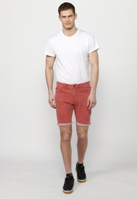Shorts de mezclilla roja con dobladillos, combinados con una camiseta blanca básica. Zapatillas negras completan el look casual.