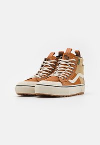Brune semskede høyhælte sneakers med hvite snørebånd, kremfarget gummisåle og svart foring. Har en kontrasterende kremfarget sidestripe og logostikke.