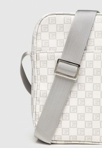 Crossbody-väska i vit och grå rutig mönster, med en strukturerad tyg, justerbar silverrem och robusta hårdvaruinslag.