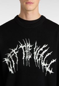 Suéter de punto negro con un diseño gráfico abstracto en blanco. Cuello redondo con textura de canalé, enfatizando una estética moderna y minimalista.
