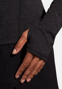 Maglietta nera a maniche lunghe con dettagli per il pollice. Tessuto morbido e texturizzato e cuciture piatte offrono comfort e un design aderente.