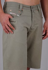 Hellgraue Cargo-Shorts mit geradem Schnitt, ausgestattet mit Kupferbeschlägen, aufgesetzten Taschen und subtilem Texturmuster. Die Vordertasche hat dekorative Stickerei.