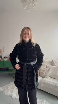 Casaco de pele preta com riscas horizontais, apresentando uma gola alta e um cinto atado. Textura suave e aparência macia, usado sobre calças pretas.