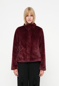 Chaqueta de pelo sintético burdeos con cuello alto, mangas largas y bolsillos laterales, que presenta una textura suave y una silueta relajada.