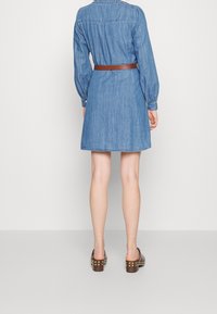 Dżinsowa sukienka z długimi rękawami, paskiem w talii i rozkloszowanym dołem. Jasnoniebieski kolor, widoczne szwy i klasyczny krój kołnierza.