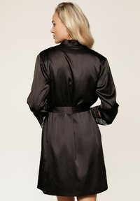Robe en satin noir avec de longues manches ornées de dentelle et une ceinture à nouer. Le dos présente un design lisse et élégant.