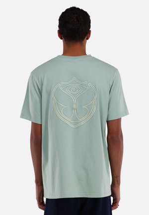 T-shirt vert menthe, manches courtes, présentant un grand motif graphique contourné en blanc au dos ressemblant à un œil à l'intérieur d'une forme de fleur.