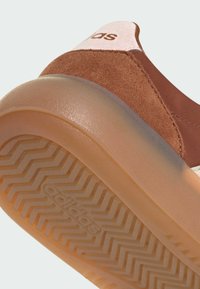 Brązowe zamszowe i tekstylne sneakersy z gumową podeszwą. Posiada różową pętelkę na pięcie i wytłoczone logo. Teksturowany wzór bieżnika na podeszwie.