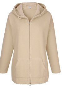 Chaqueta de forro polar beige con capucha, cierre de cremallera en la parte delantera, dos bolsillos frontales y una superficie texturizada suave. Corte holgado con mangas largas.