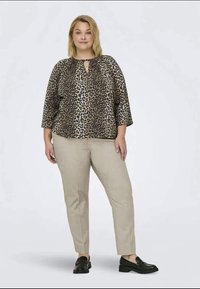 T-shirt de estampado de leopardo com decote redondo e mangas três quartos, combinada com calças bege. Ambos são feitos de um tecido leve.