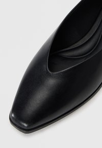 Escarpin en cuir noir avec un bout pointu et un design découpé. Texture lisse avec un éclat subtil et une doublure intérieure noire élégante.