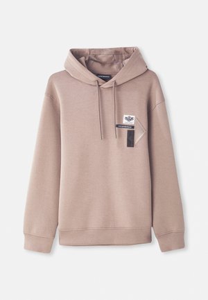 Beige spalvotas džemperis su kapu, turintis priekinę kišenę su logotipų užpatch'ais. Sukurtas su laisvu kirpimu ir ribotu rankogaliu bei apačia. Lygus tekstūra.